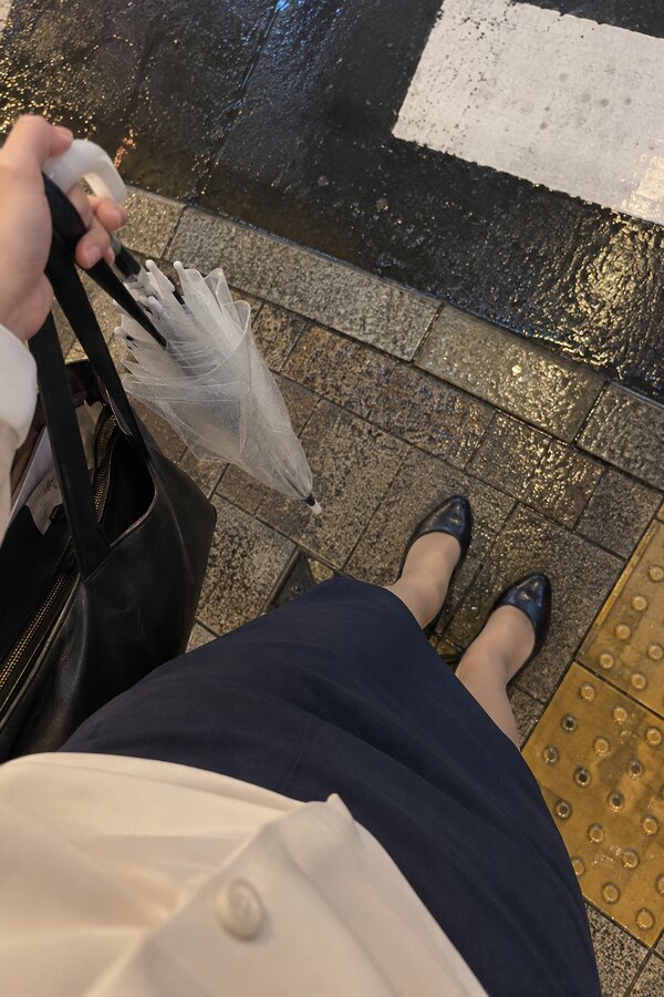 雨上がりの横断歩道で通勤バッグと折り畳んだ傘を持つなみの左手